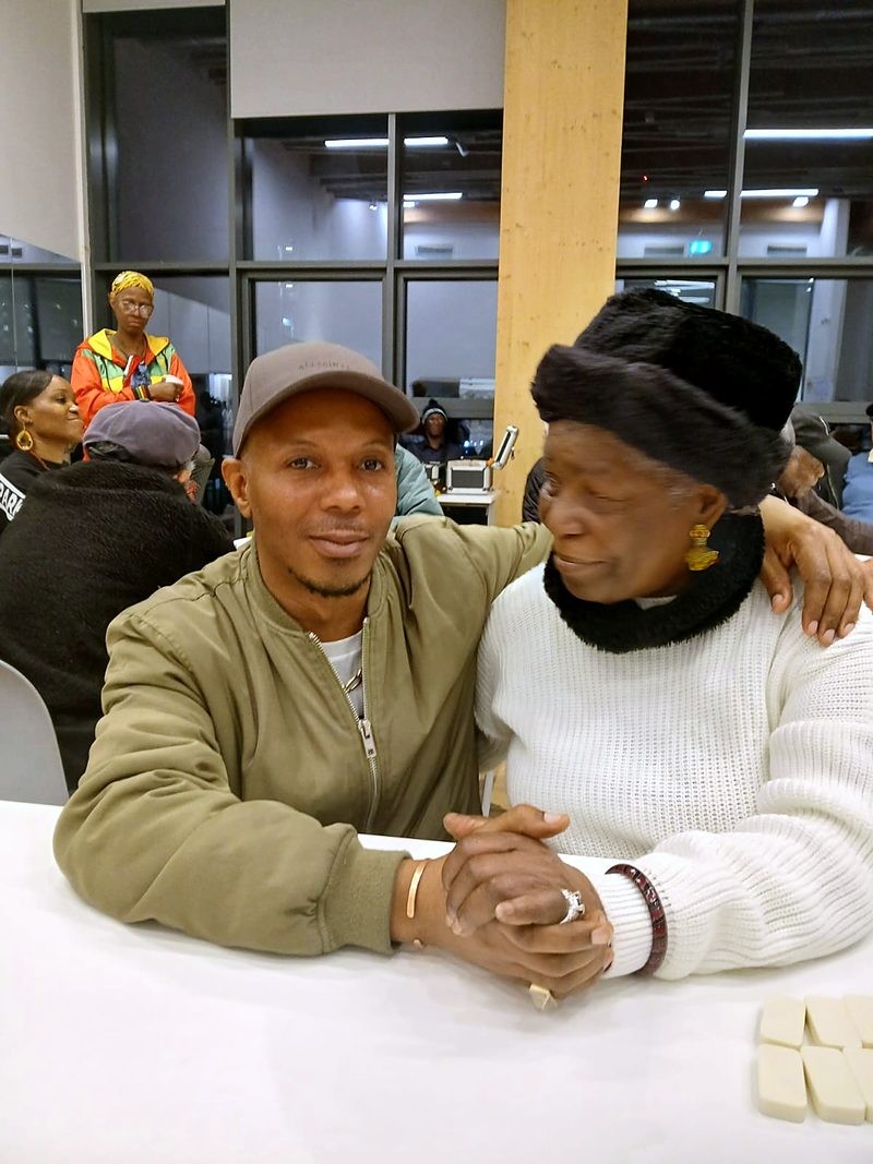 Nathan sitting with an elder at a community dominoes evening, both smiling