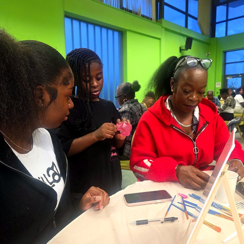 Two young people and an older woman working together at a community craft table